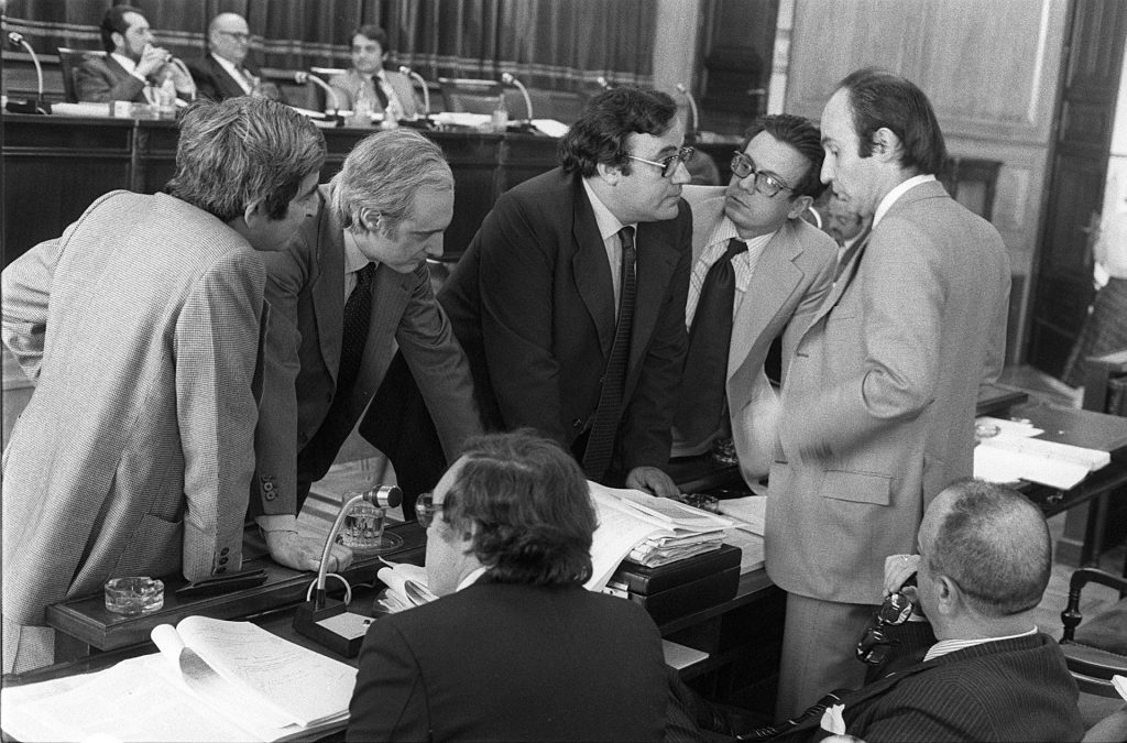 Madrid, 16/05/1978.- La Comisión Constitucional ha debatido hoy el artículo 7 del proyecto de la Constitución, referente a las asociaciones sindicales y empresariales. En la imagen, Gabriel Cisneros, José Pedro Pérez Llorca, Gregorio Peces Barba, Miguel Herrero y Miquel Roca, discuten las posiciones, en presencia de Jordi Solé Tura y Manuel Fraga (sentados, de espaldas), antes de proceder a la votación. EFE/jgv
