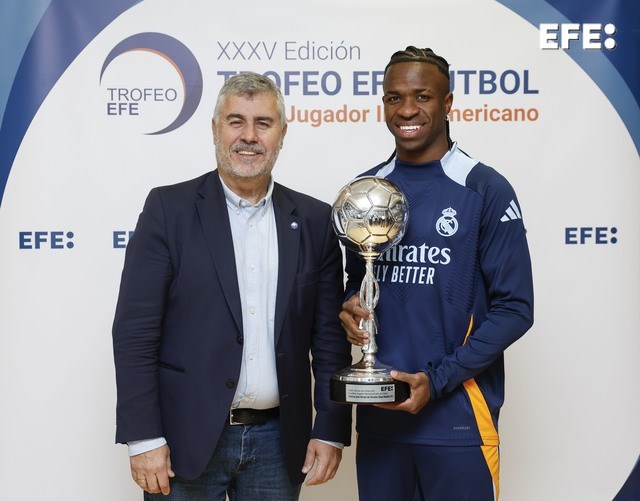 Madrid, 31/12/2024.- El delantero brasileño del Real Madrid Vinícius jr. (d), acompañado por el presidente de la Agencia EFE, Miguel Ángel Oliver (i), posa con el Trofeo EFE al Mejor Jugador Iberoamericano de Fútbol antes de participar en el entrenamiento realizado en Valdebebas, tras regresar al trabajo después del descanso navideño. EFE